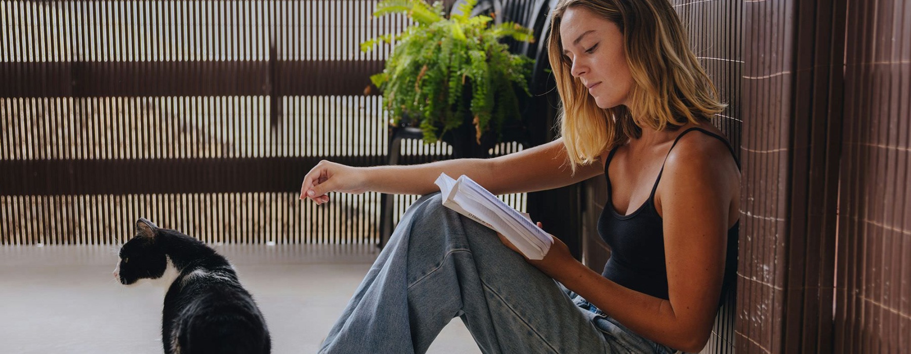 A woman sitting on a patio reading with her cat.